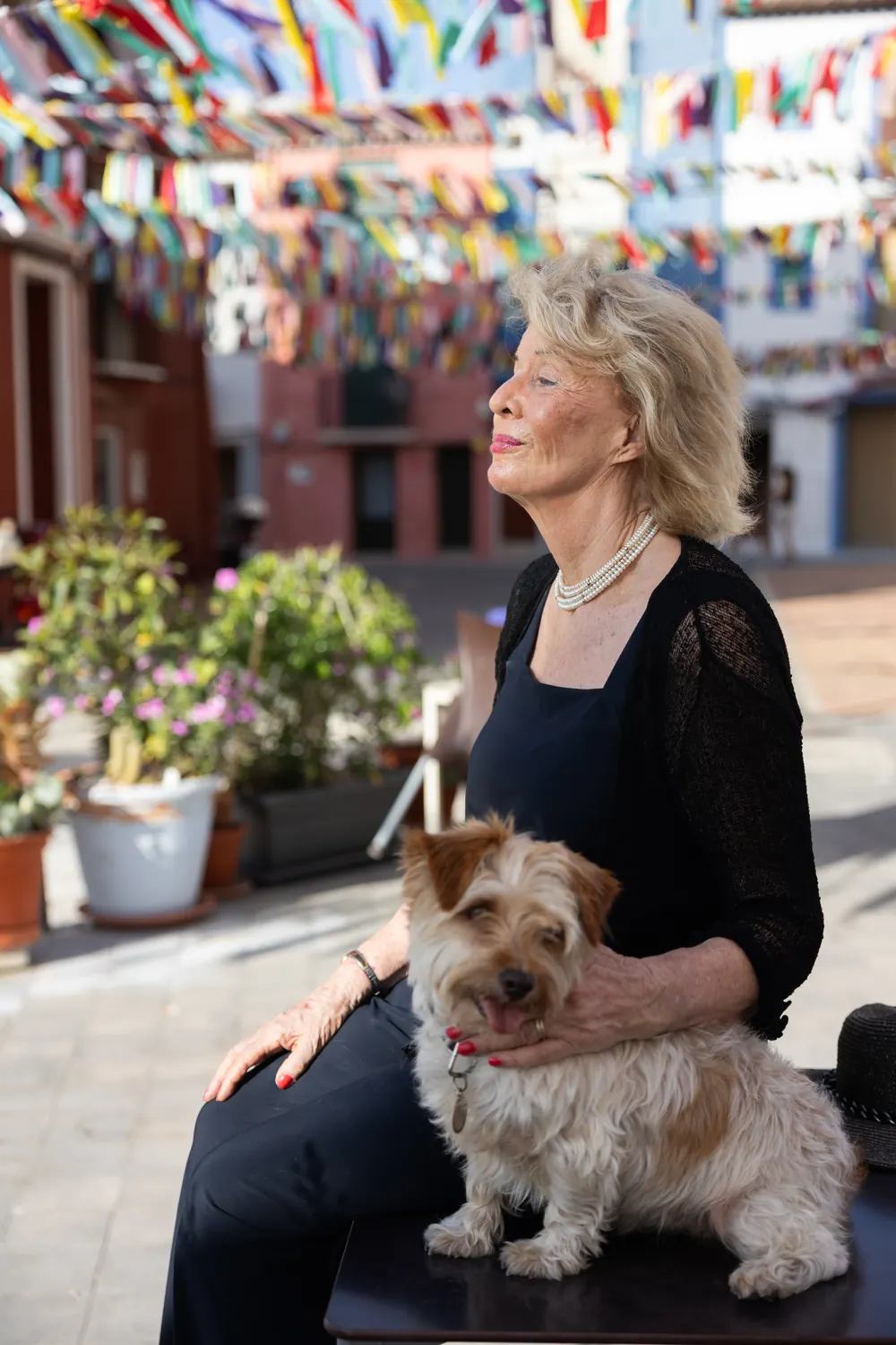 Jessica Larive in het zwart met haar hond op schoot, in een straat vol vlaggetjes