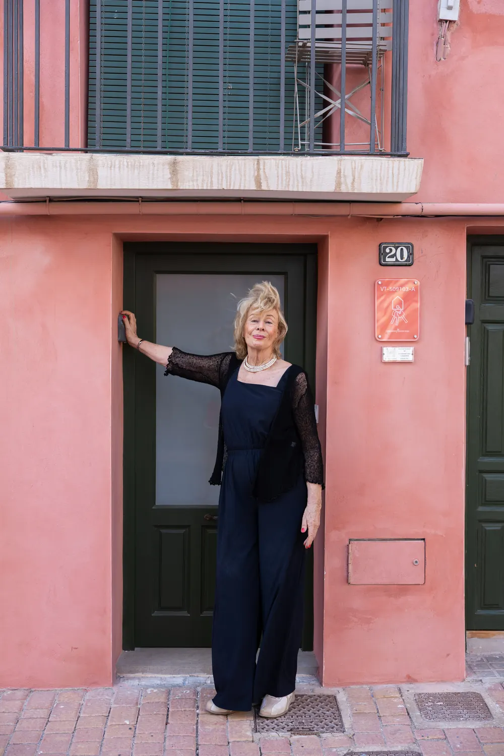 Jessica Larive in het zwart in een deuropening van een roze huis