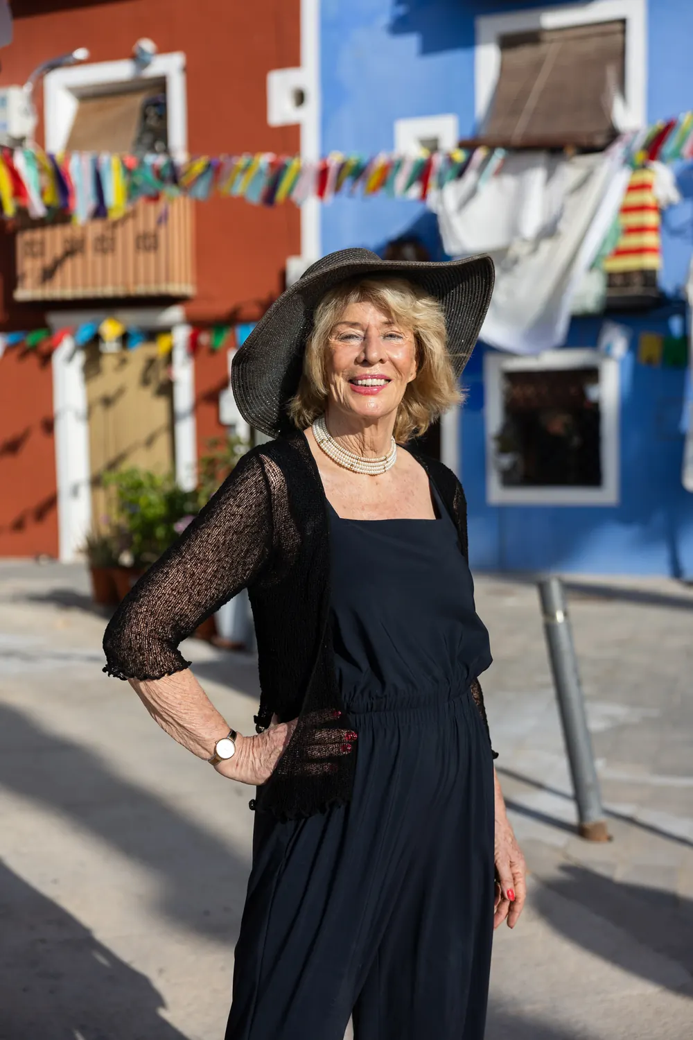 Jessica Larive lacht in een straat vol vlaggetjes, in het zwart met een zwarte hoed