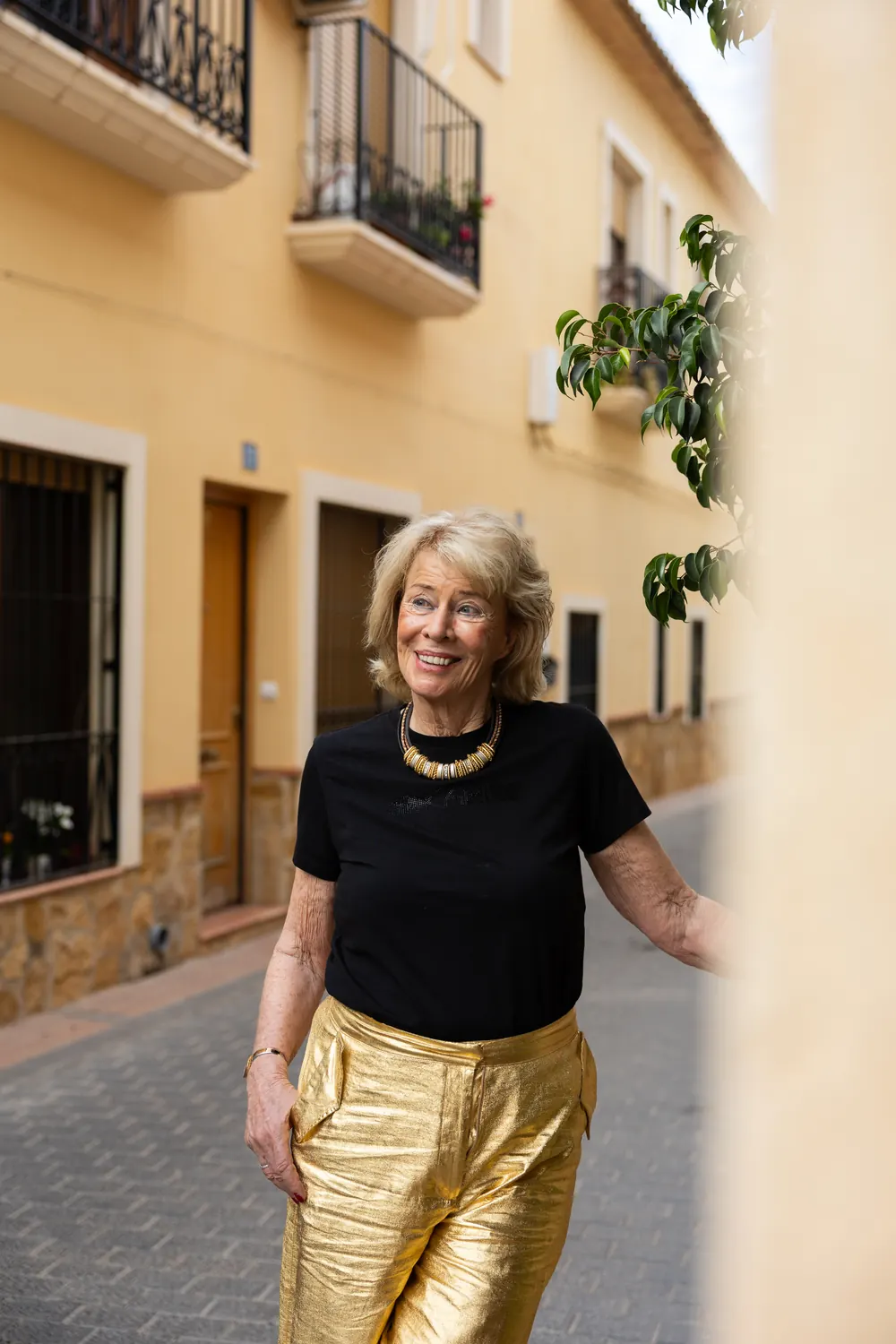 Jessica Larive lacht in een smalle straat, in een zwart shirt met een gouden ketting
